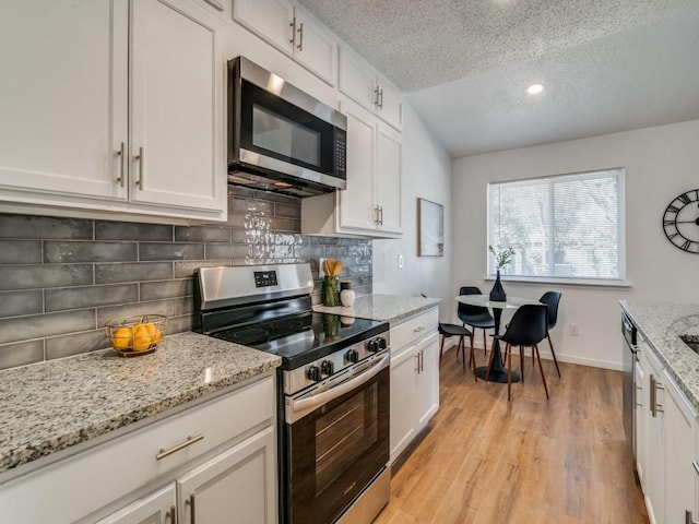 kitchen featuring white cabinetry, light stone counters, a textured ceiling, decorative backsplash, and appliances with stainless steel finishes