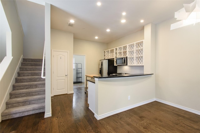 kitchen with appliances with stainless steel finishes, dark hardwood / wood-style floors, kitchen peninsula, white cabinets, and backsplash