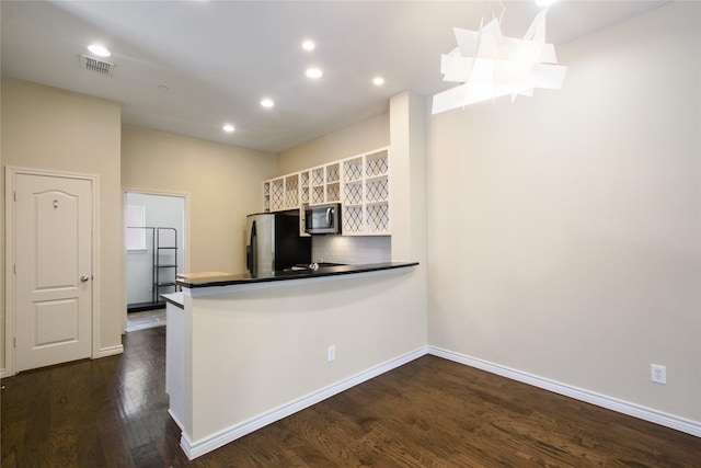 kitchen with appliances with stainless steel finishes, white cabinets, backsplash, dark hardwood / wood-style flooring, and kitchen peninsula