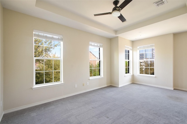 empty room with a raised ceiling, light colored carpet, and ceiling fan