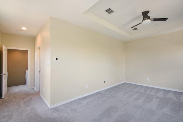 unfurnished room with a raised ceiling, light colored carpet, and ceiling fan