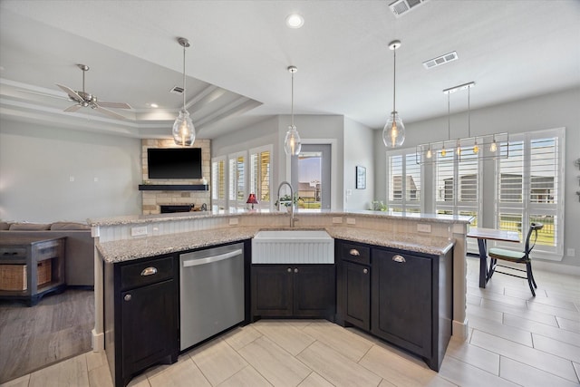 kitchen with ceiling fan, dishwasher, sink, a tray ceiling, and a center island with sink