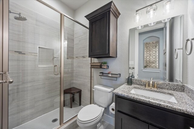 bathroom featuring a shower with door, vanity, and toilet