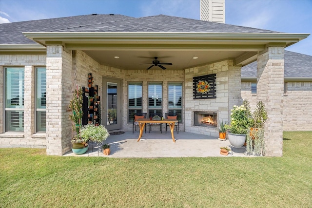 rear view of property with ceiling fan, a yard, a patio, and an outdoor stone fireplace