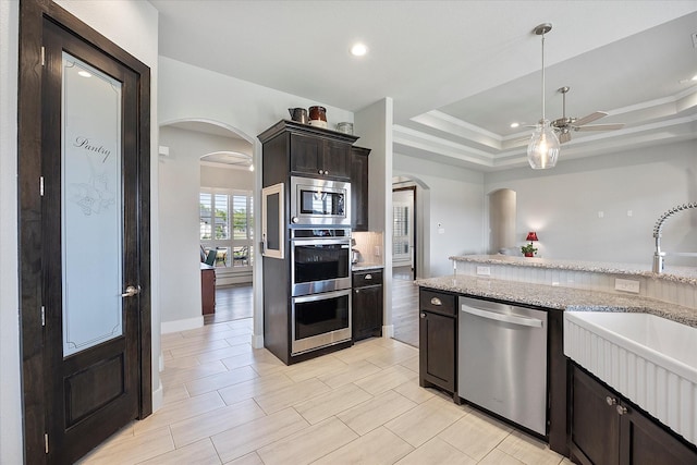 kitchen featuring a raised ceiling, sink, light stone countertops, dark brown cabinetry, and stainless steel appliances