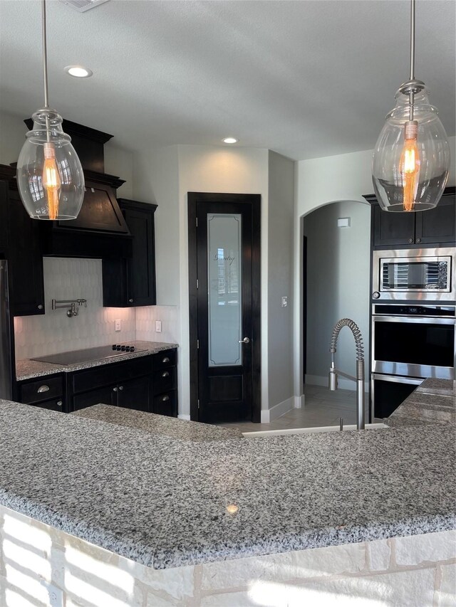 kitchen featuring tasteful backsplash, light stone counters, hanging light fixtures, and black appliances