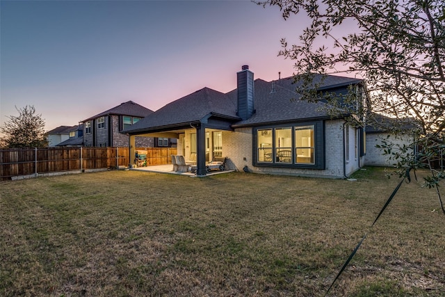 back house at dusk featuring a yard and a patio area