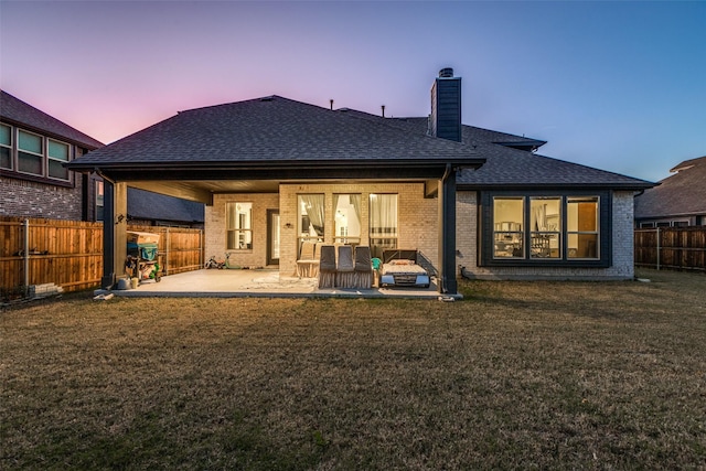 back house at dusk featuring a patio area and a lawn