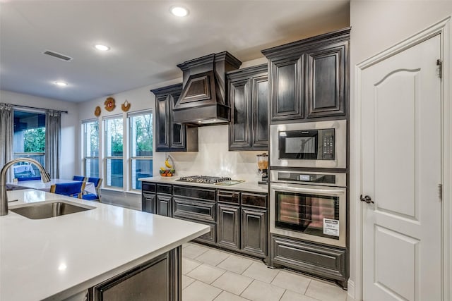 kitchen with sink, custom exhaust hood, light tile patterned floors, appliances with stainless steel finishes, and decorative backsplash