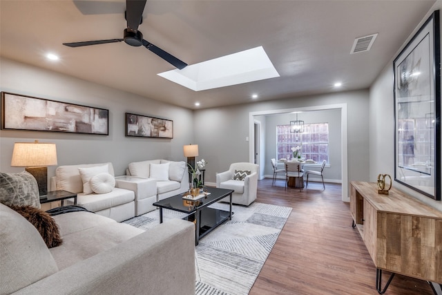 living room with wood-type flooring, ceiling fan with notable chandelier, and a skylight