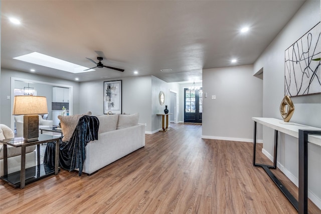 living room featuring wood-type flooring, ceiling fan with notable chandelier, a skylight, and french doors