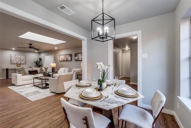 dining room with light wood-type flooring, ceiling fan with notable chandelier, and a skylight