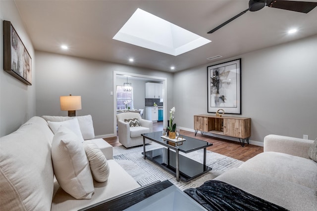 living room featuring hardwood / wood-style flooring, ceiling fan, and a skylight