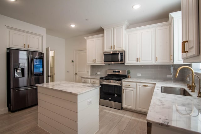 kitchen featuring light stone countertops, appliances with stainless steel finishes, sink, white cabinets, and a kitchen island