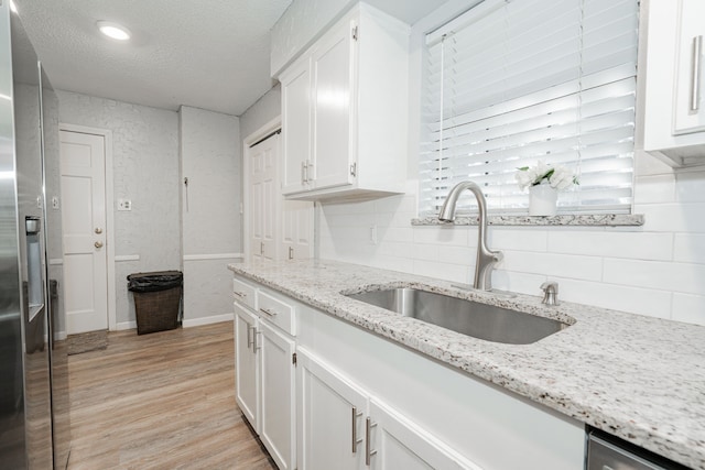 kitchen featuring white cabinetry, sink, stainless steel fridge with ice dispenser, light hardwood / wood-style floors, and a textured ceiling