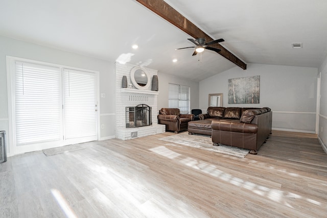 living room with ceiling fan, a brick fireplace, vaulted ceiling with beams, plenty of natural light, and light wood-type flooring