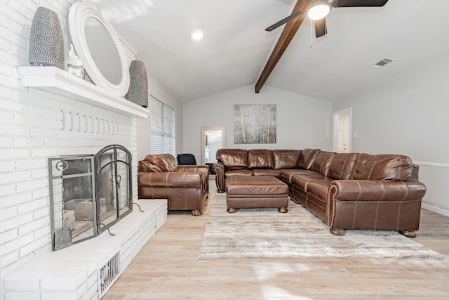 living room featuring ceiling fan, light hardwood / wood-style floors, lofted ceiling with beams, and a brick fireplace