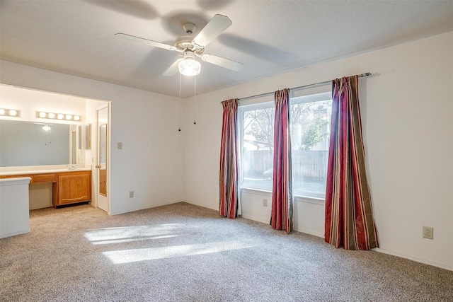 unfurnished bedroom featuring connected bathroom, built in desk, light colored carpet, and ceiling fan