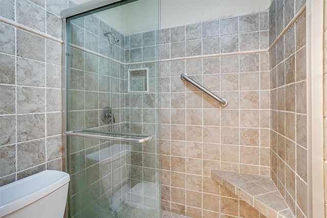 bathroom featuring a shower with door and toilet