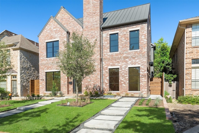 view of front of home featuring a chimney, metal roof, a standing seam roof, a front lawn, and brick siding