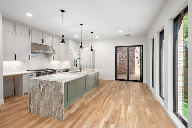 kitchen featuring sink, decorative light fixtures, light stone counters, and an island with sink