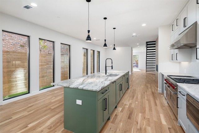 kitchen featuring light stone countertops, a kitchen island with sink, sink, hanging light fixtures, and green cabinets