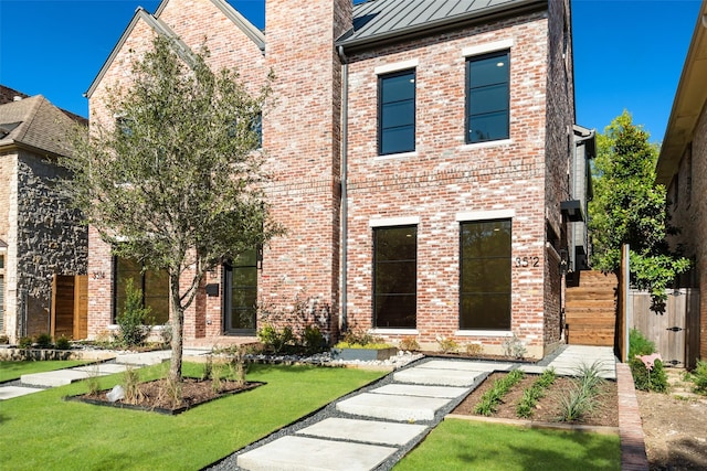 view of front of property with a front yard, a standing seam roof, brick siding, and metal roof