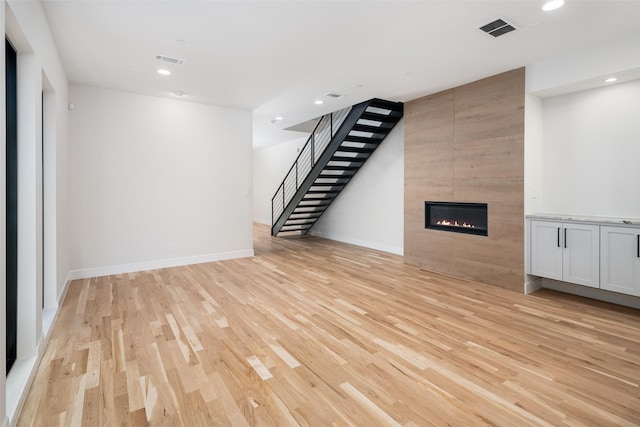 unfurnished living room with light wood-type flooring and a tiled fireplace