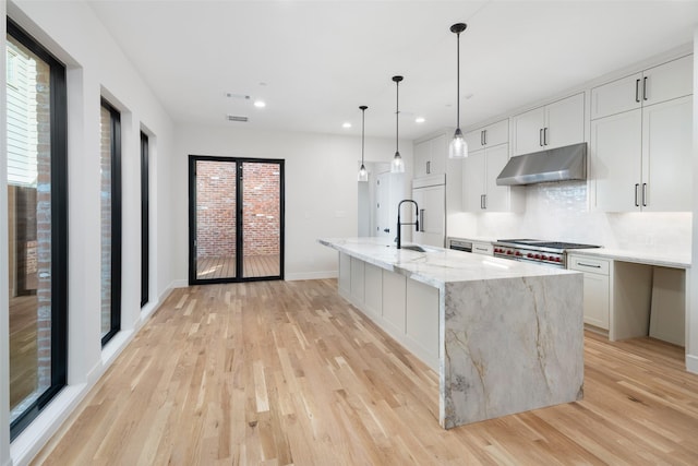 kitchen featuring light stone countertops, backsplash, a center island with sink, light hardwood / wood-style floors, and white cabinetry