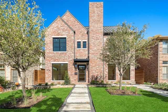 view of front of home with a chimney, metal roof, a standing seam roof, a front yard, and brick siding