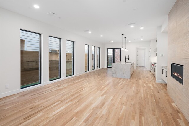 unfurnished living room featuring a tiled fireplace, sink, and light wood-type flooring