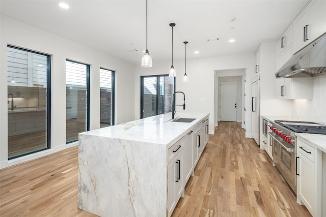 kitchen with white cabinetry, sink, light stone counters, and a center island with sink