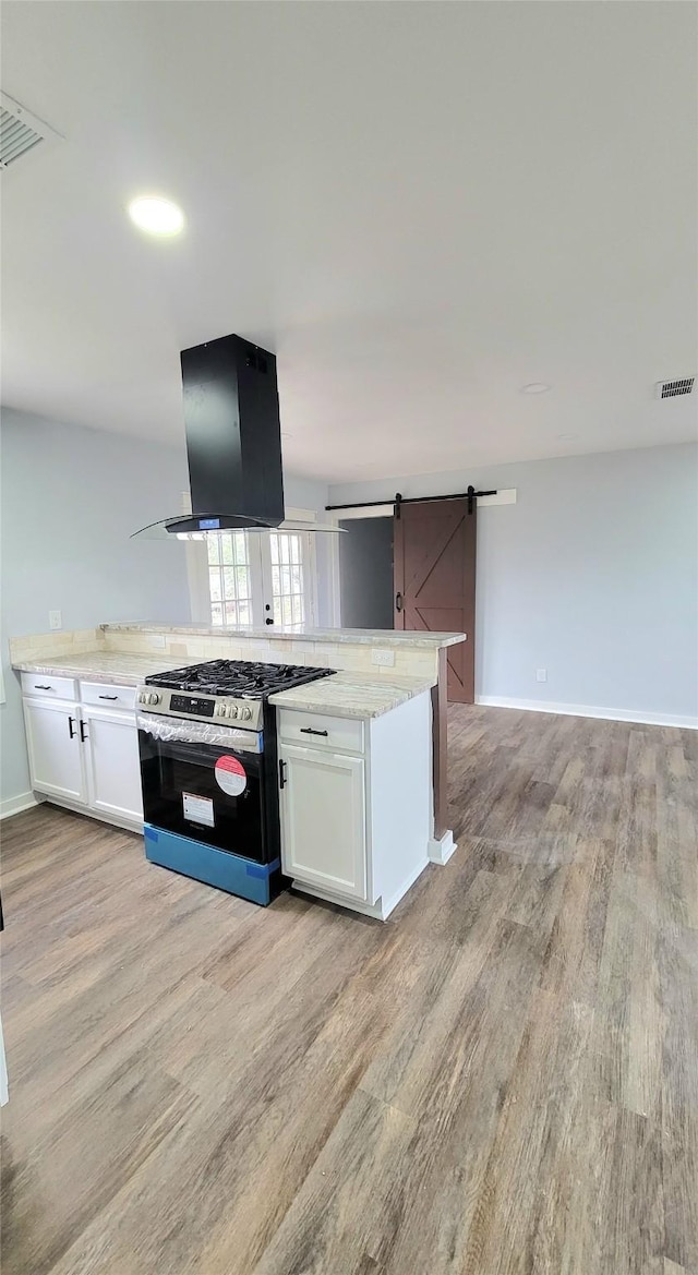 kitchen with a barn door, visible vents, light wood-type flooring, stainless steel range with gas cooktop, and island exhaust hood