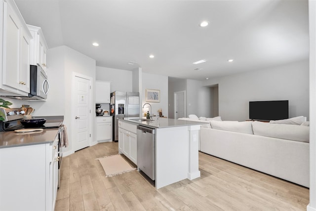 kitchen with appliances with stainless steel finishes, open floor plan, white cabinets, a sink, and an island with sink