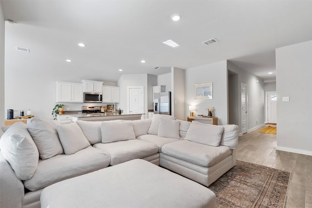 living area featuring baseboards, light wood finished floors, visible vents, and recessed lighting