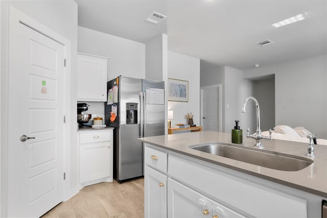 kitchen featuring white cabinets, stainless steel fridge, light wood-type flooring, and sink