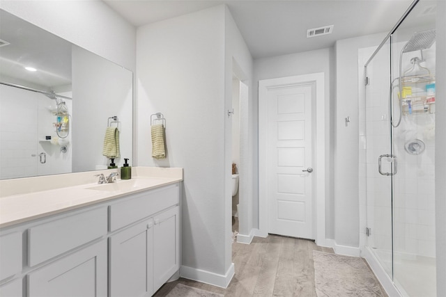 bathroom featuring toilet, vanity, an enclosed shower, and hardwood / wood-style flooring