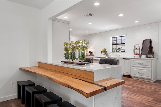 kitchen featuring dark wood-type flooring, a breakfast bar, butcher block counters, white cabinets, and kitchen peninsula