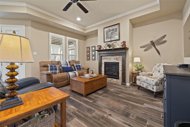 living room featuring ceiling fan, ornamental molding, dark hardwood / wood-style floors, and a stone fireplace