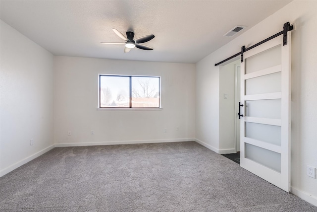 unfurnished bedroom with a barn door, ceiling fan, a textured ceiling, and dark colored carpet