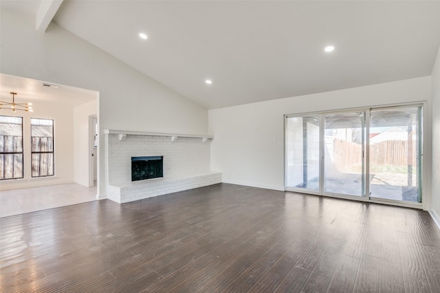 unfurnished living room with a chandelier, a healthy amount of sunlight, a brick fireplace, and beamed ceiling