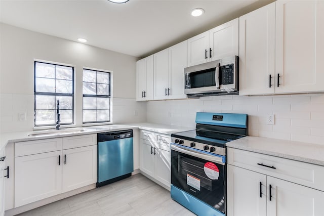 kitchen with light stone countertops, sink, stainless steel appliances, decorative backsplash, and white cabinets