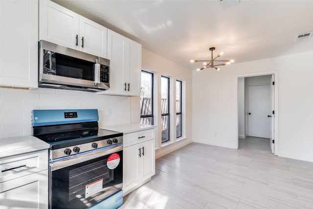 kitchen with tasteful backsplash, white cabinetry, stainless steel appliances, and a notable chandelier