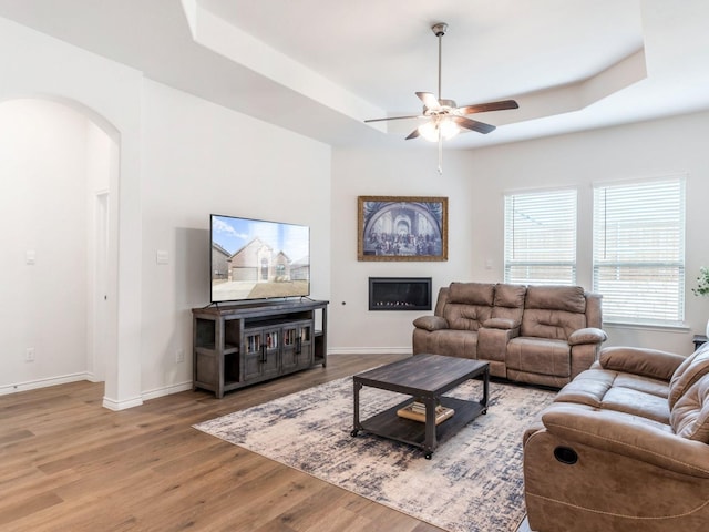 living room with wood-type flooring, a raised ceiling, and ceiling fan