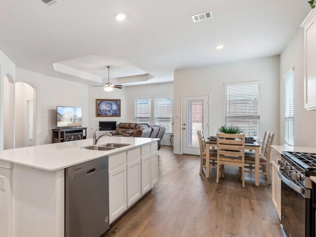 kitchen featuring stainless steel appliances, a tray ceiling, sink, a center island with sink, and white cabinetry