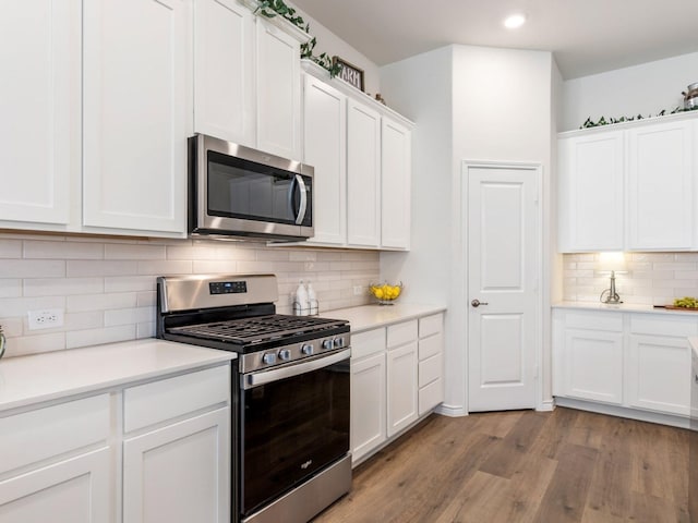 kitchen with tasteful backsplash, white cabinets, light wood-type flooring, and appliances with stainless steel finishes