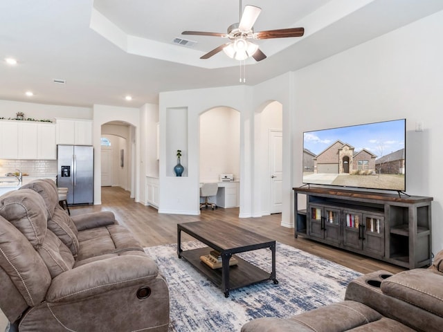 living room with hardwood / wood-style floors, a raised ceiling, ceiling fan, and sink