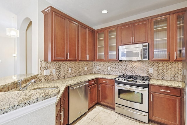 kitchen with pendant lighting, backsplash, light stone countertops, light tile patterned floors, and stainless steel appliances