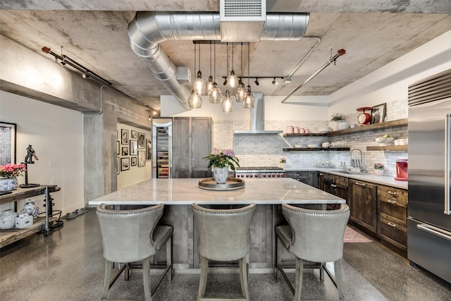 kitchen featuring built in fridge, sink, wall chimney exhaust hood, and a kitchen island