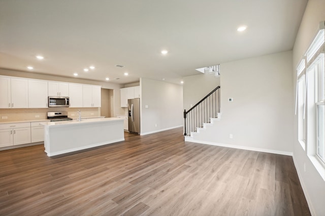 kitchen featuring a kitchen island with sink, light hardwood / wood-style flooring, decorative backsplash, white cabinetry, and stainless steel appliances